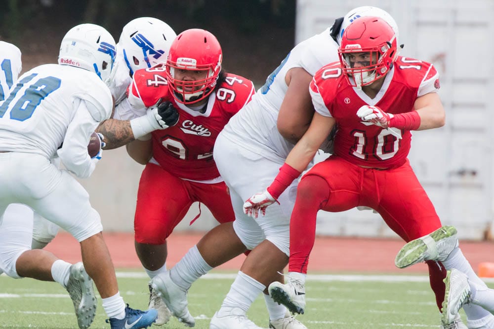 Ram’s defensive linemen Uhi Mikaele (#94) and Kobie Beltram (#10) bust through the San Mateo offensive line as they attempt to bring down the ball carrier. Photo by Peter Wong.