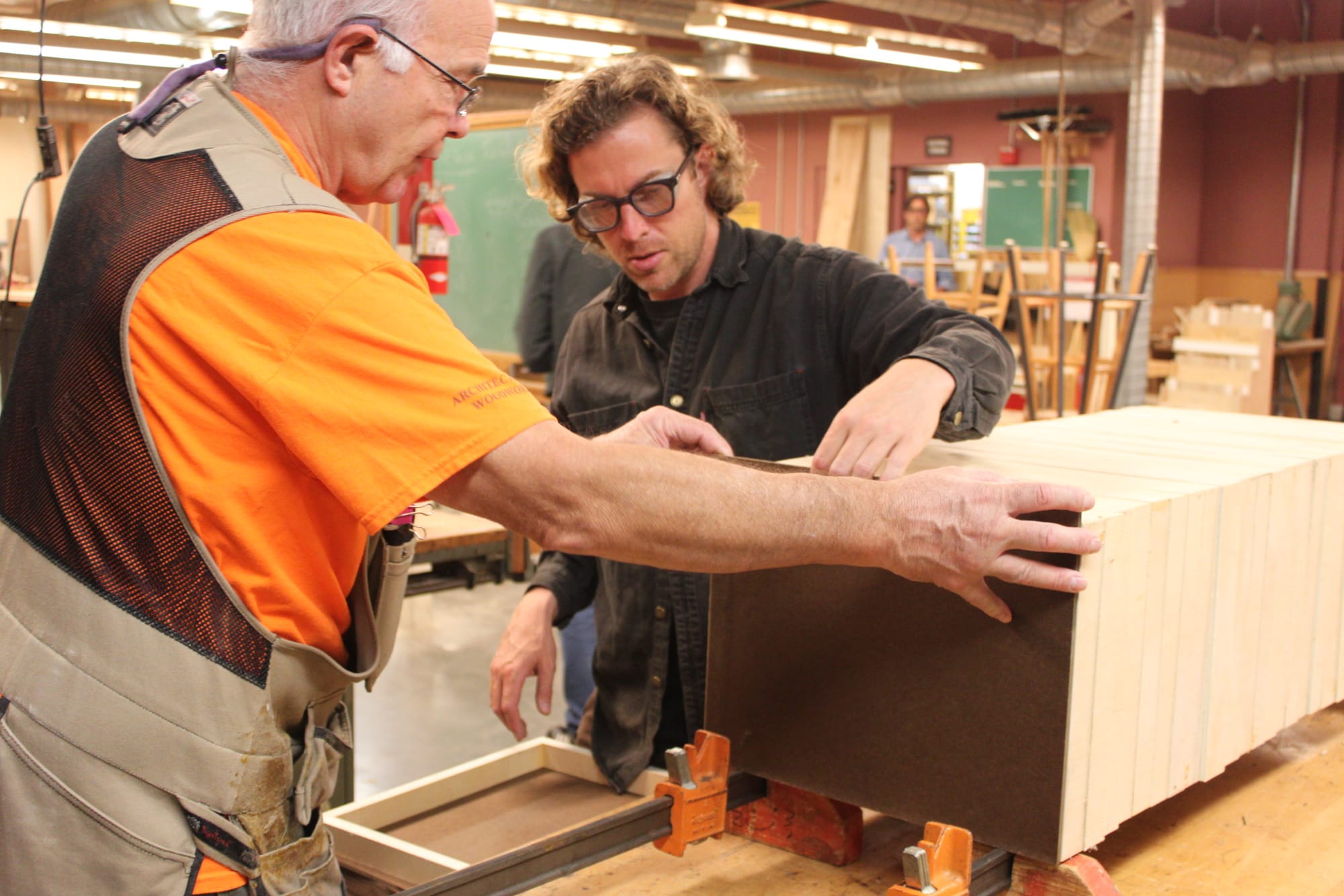 City college student Trevor Rogers creates a variety of projects. Instructing how to clamp and glue Rogers’ wooden frames is Raymond Cash. Rogers is an artist who hopes to create several of the enclosed frames to further paint. A project that Rogers said would be much more difficult and costly if not for his class. Photo taken by Bethaney Lee on Nov. 6, 2017. 
